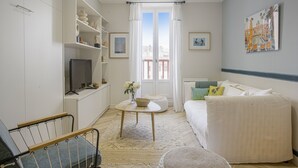 Une chambre moderne et bien éclairée, équipée d’un lit, d’une télévision, d’une bibliothèque et offrant une vue sur l’extérieur par une fenêtre.