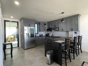A modern kitchen with grey cabinets, stainless steel appliances, and a central island with bar stools. - Resort Don Julian - Unit 2 (La Libertad)
