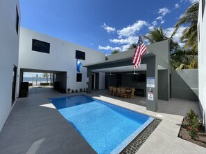A modern outdoor pool area with a clear blue pool, a covered seating area, and an American flag.