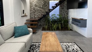 Una sala de estar moderna con un sofá gris, una mesa de centro de madera y una escalera que conduce a un balcón.