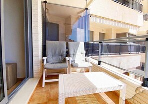 A balcony with two chairs and a small table, a glass door, and a view of the building's exterior.