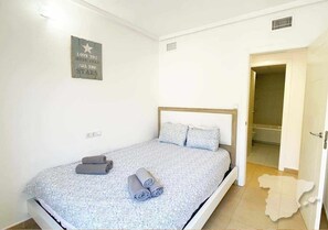 Une chambre à coucher avec un lit, des oreillers, un tableau accroché au mur et une porte ouverte donnant sur une salle de bain.