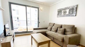 Een woonkamer met een bank, een houten salontafel, een televisie op een meubel en een schuifdeur naar een buitenruimte.