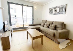 A living room with a sofa, a wooden coffee table, a TV on a stand, and a sliding glass door leading to an outdoor area.