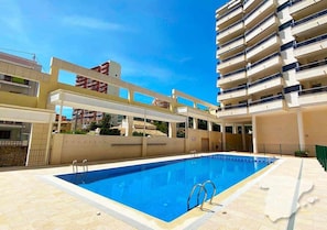 A swimming pool with two ladders, surrounded by a light-colored tiled deck.