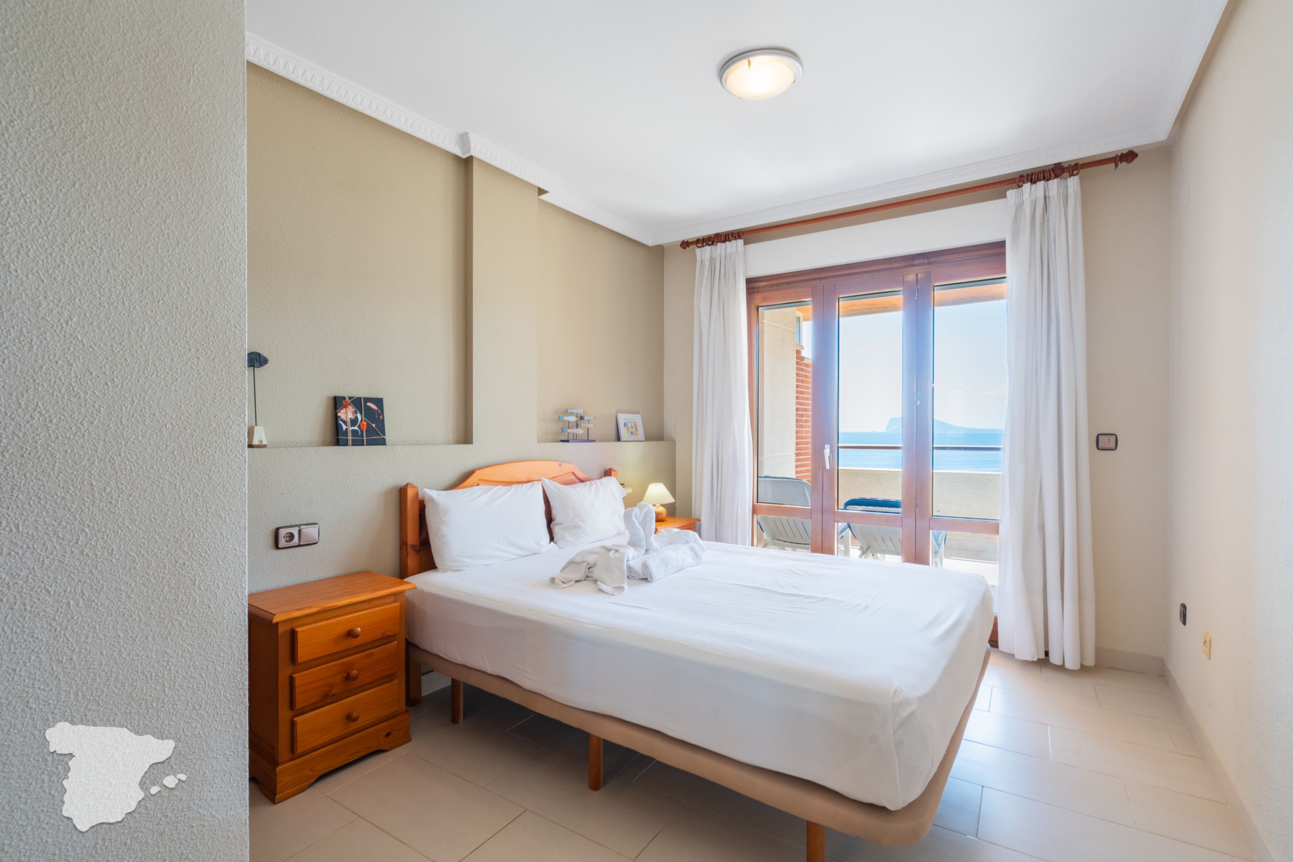 A hotel room with a bed, a nightstand, a lamp, a window with curtains, and a view of the outside.