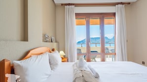 Una camera d'albergo con un letto, un comodino, una lampada e vista sulla spiaggia e sulle montagne attraverso la finestra.