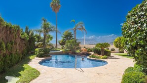 Una piscina con un percorso in pietra, circondata da vegetazione e palme.