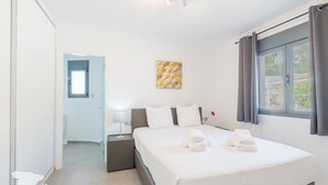 Una habitación de hotel moderna con una cama grande, una mesita de noche, una lámpara y un ventanal con cortinas.