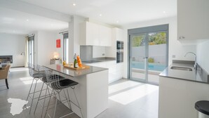 Una cocina moderna con armarios blancos, una isla central con taburetes, horno integrado y vistas a una piscina.