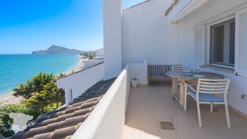 A balcony with a table and chairs, overlooking a beach and the sea.