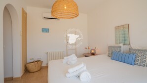 Un dormitorio con una cama grande, una lámpara colgante de mimbre, aire acondicionado de pared, una cesta y una cita inspiradora en un marco.