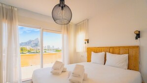 A hotel room with a large bed, wooden headboard, and a view of a cityscape through the balcony. - CostaBlancaDreams - Casa Colari 4 in Calpe (Calpe)