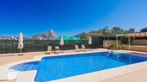 A swimming pool with lounge chairs and umbrellas, a stone wall, and a view of a mountain. - CostaBlancaDreams - Casa Colari 4 in Calpe (Calpe)