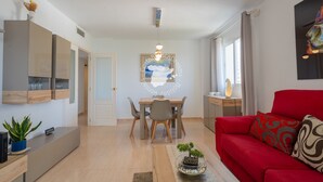 A modern living room with a red sofa, a dining table with chairs, a kitchen area with cabinets, and a large window with curtains. - CostaBlancaDreams - Apolo 12, 4e in Calpe (Calpe)