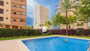 A swimming pool with a person swimming, surrounded by greenery and a tall building in the background. - CostaBlancaDreams - Apolo 12, 4e in Calpe (Calpe)