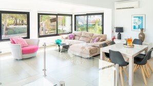 A modern living room with a sofa, a dining table with chairs, and large windows with a view of greenery. - CostaBlancaDreams - Mila in Benissa (Calpe)