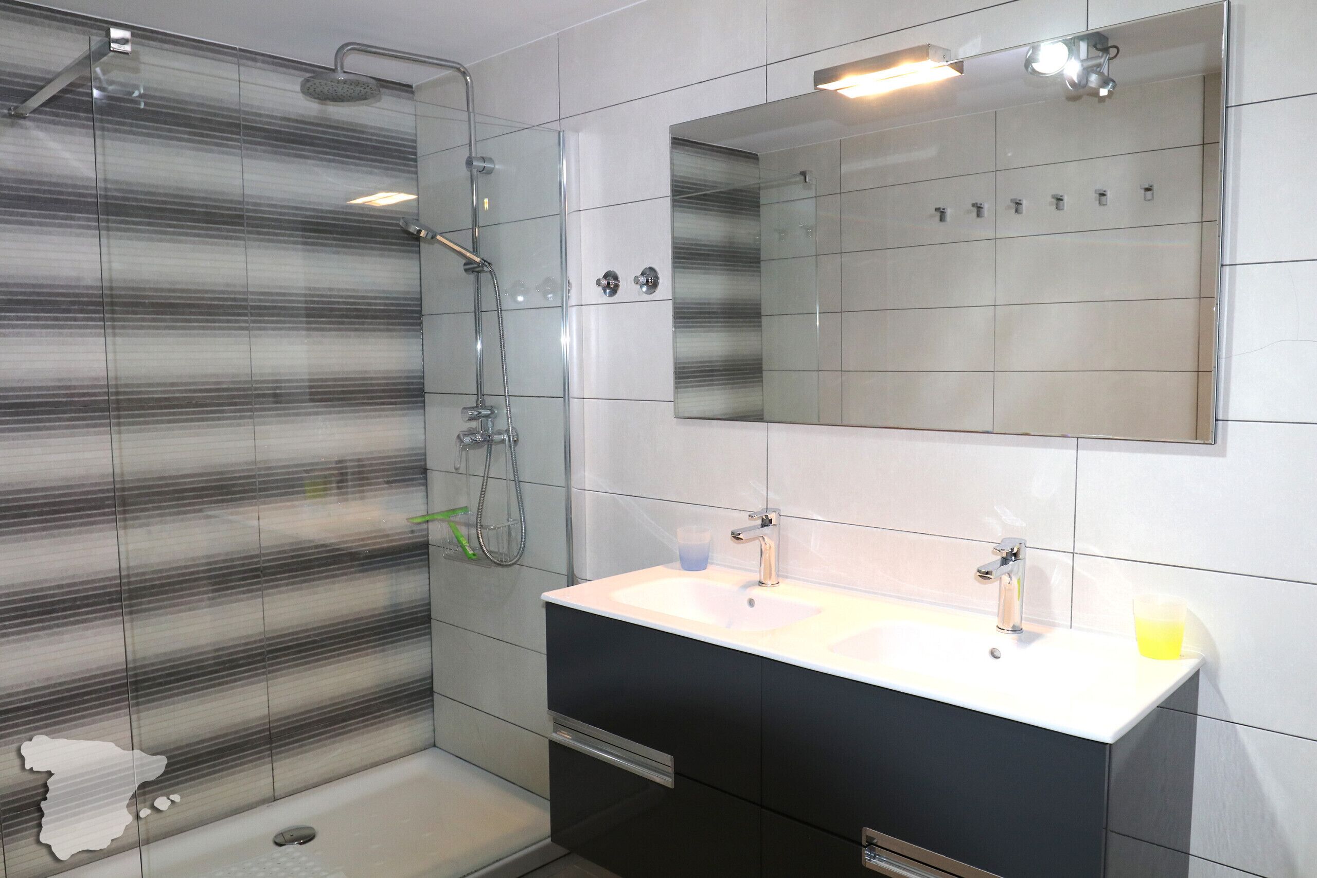 A modern bathroom with a glass shower enclosure, a large mirror, and a white sink with a black cabinet.
