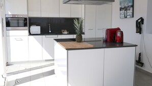 Une cuisine moderne avec des meubles blancs, un plan de travail en bois, une machine à café rouge et un ananas.