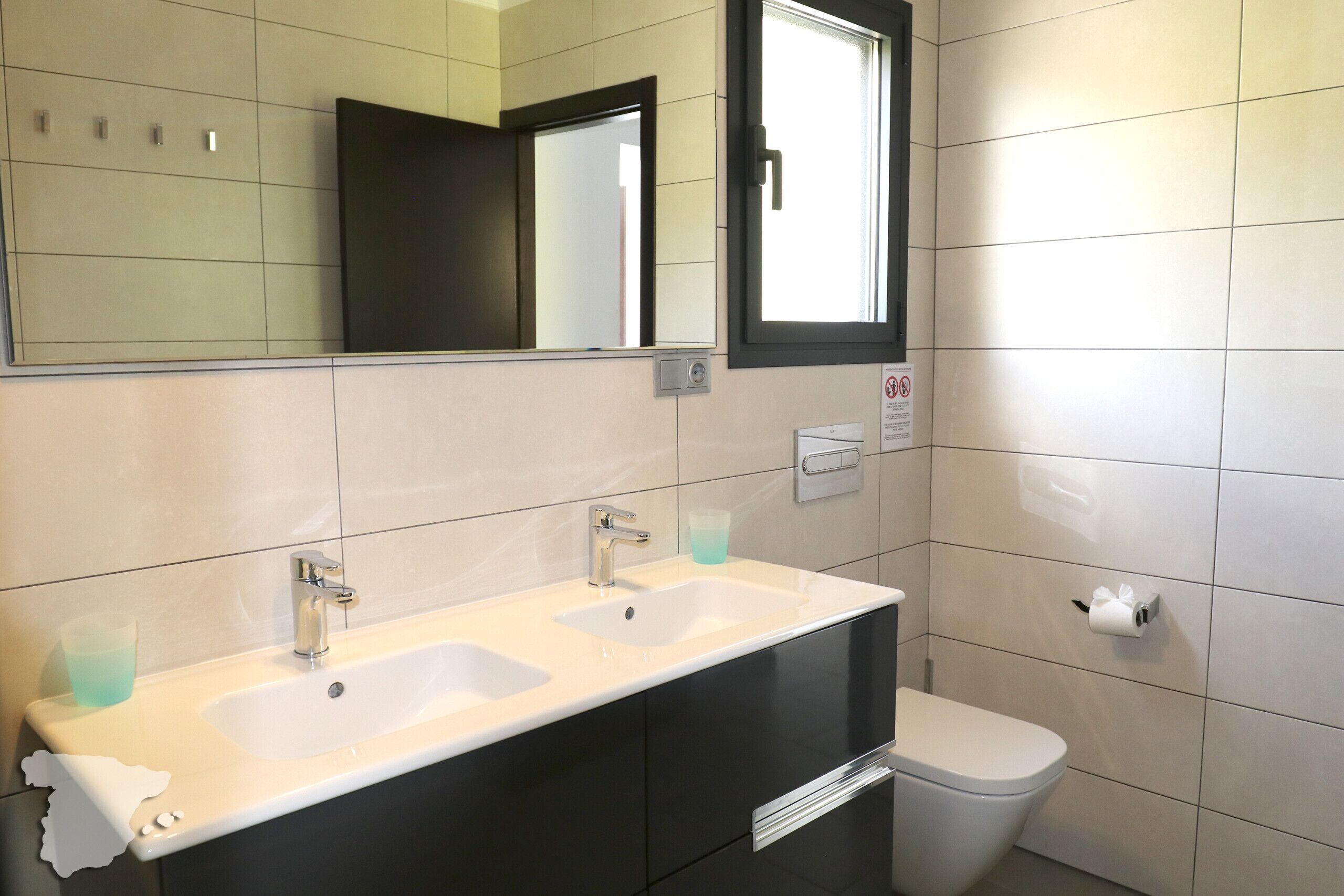 Une salle de bain avec un lavabo blanc, un miroir, des toilettes et une fenêtre.