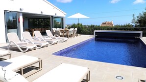 Un espace piscine avec des chaises longues et une table, une entrée avec une porte vitrée et une vue sur le paysage.