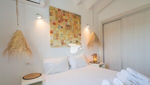 Habitación de hotel con cama, almohadas blancas, una obra de arte en la pared, lámpara de noche y un perchero para toallas.
