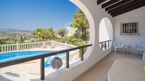 Un balcón con piscina, sillas blancas y vistas al paisaje.