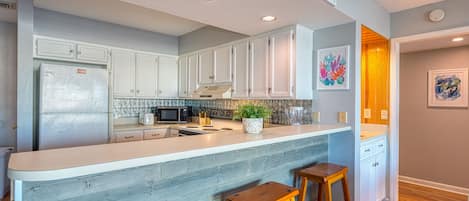 A modern kitchen with white cabinets, a granite countertop, and wooden stools.