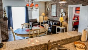 A modern kitchen with granite countertops, a dining area with a round table and chairs, a black leather sofa, and a brick wall. - One Bedroom Lakeside, Luxury Condo, Branson, MO 3211261 (Branson)