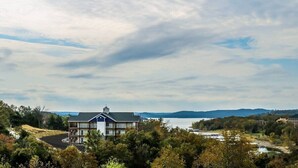 A two-story building with a balcony, surrounded by trees and a body of water in the background. - One Bedroom Lakeside, Luxury Condo, Branson, MO 3211261 (Branson)