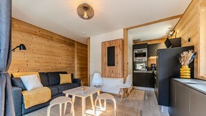 Ein modernes Wohnzimmer mit Sofa, Couchtisch und Sesseln, ein Küchenbereich mit Geräten und einer Holzwand.