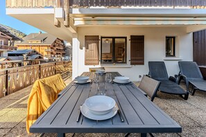 Un espace de restauration en plein air avec une table dressée pour quatre personnes, entourée de chaises, et une serviette jaune posée sur un banc.