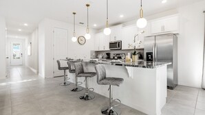 Una cocina moderna con armarios blancos, electrodomésticos de acero inoxidable y tres taburetes de bar.