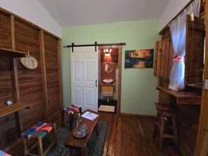 A rustic room with wooden walls, a door leading to a bathroom, a bench, a table with a bottle, and a painting on the wall. - The Lighthouse Retreat, Little Corn island, Nicaragua (Corn Islands)