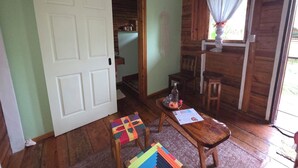 A room with a wooden floor, a white door, a wooden table with a bottle and a menu, and a window with curtains.