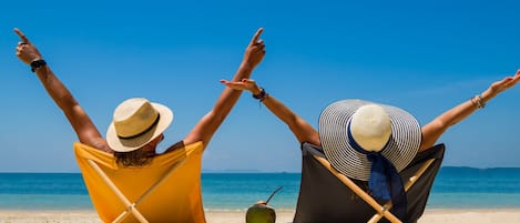 Two people sitting on beach chairs facing the sea, with their arms raised.
