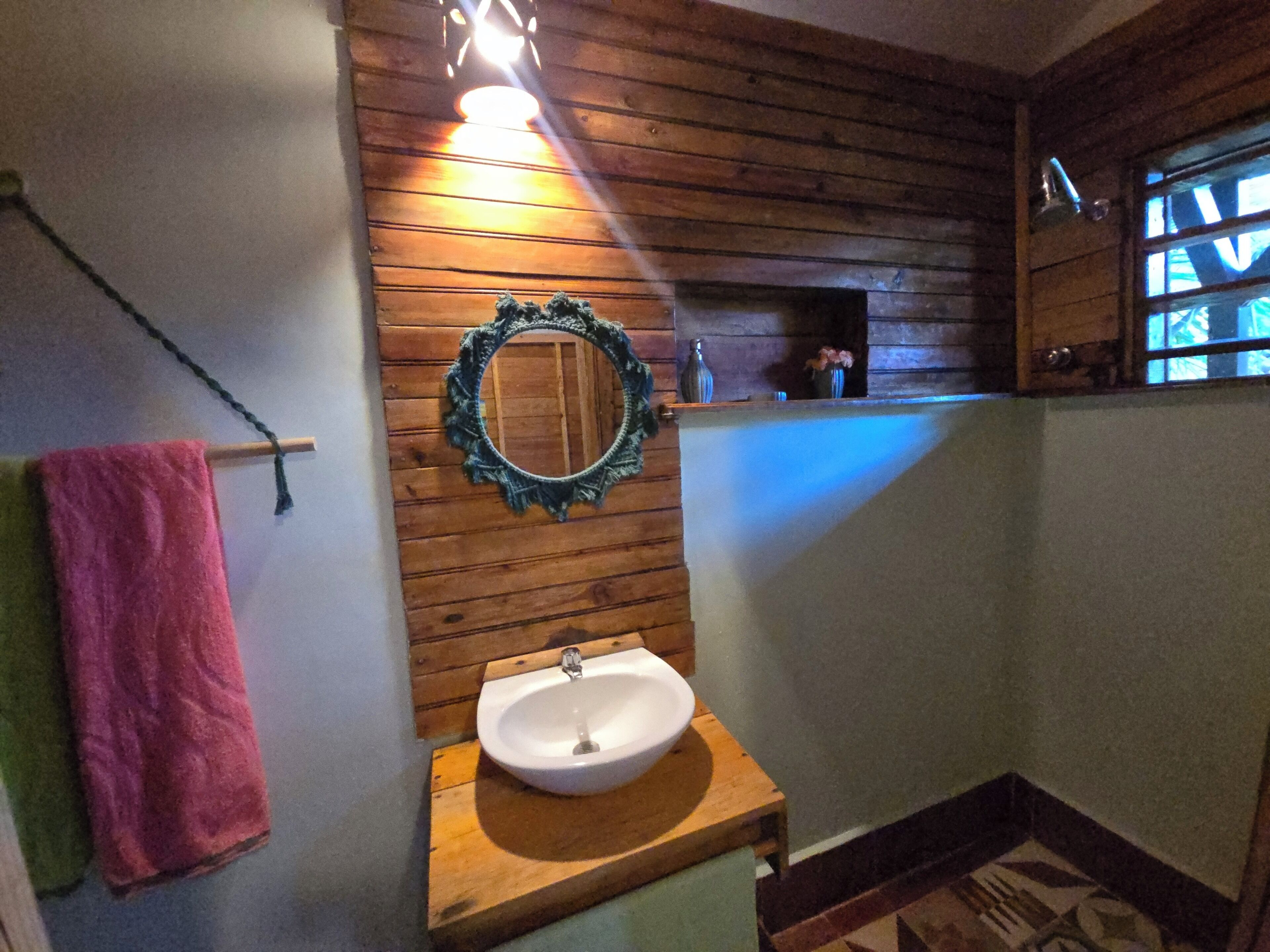 Une salle de bain avec des lambris en bois, un lavabo, un miroir et une fenêtre.