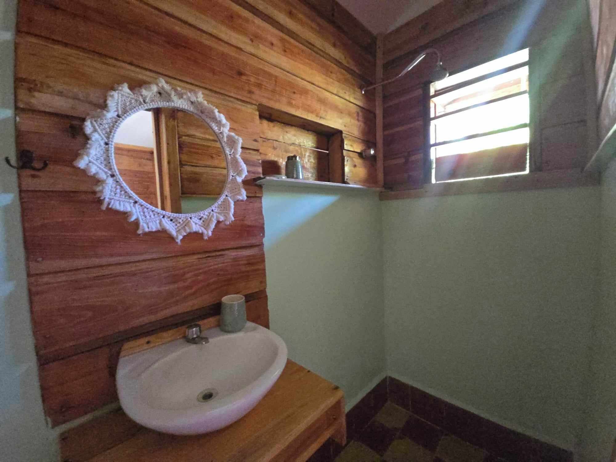 Een houten interieur met een ronde spiegel, een wastafel en een raam.
