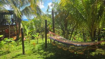 A hammock in a lush garden with a wooden structure in the background.