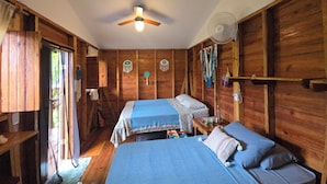 A room with two beds, wooden walls, a ceiling fan, and a window.