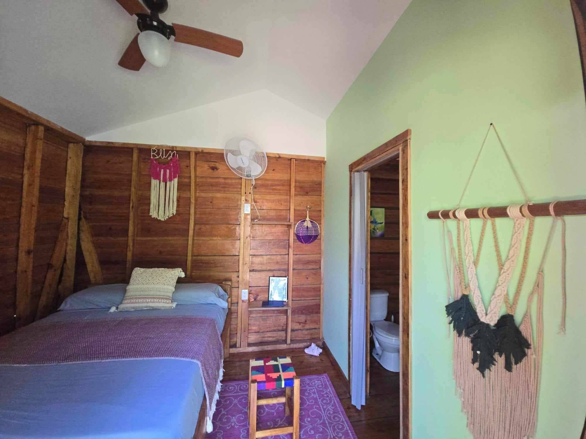 A room with two beds, a ceiling fan, a wall-mounted fan, a small table with a laptop, and a hammock.
