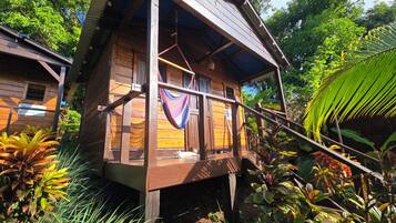 A wooden cabin with a balcony, surrounded by lush tropical vegetation.