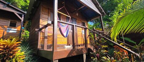 A wooden cabin with a balcony, surrounded by lush tropical vegetation.