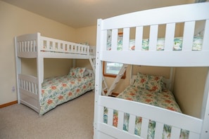 A room with bunk beds, carpeted floor, and a window with blinds.