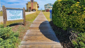 Un sentiero di legno conduce a una zona di spiaggia, con un cartello che indica l'accesso alla spiaggia riservato ai titolari di permesso.