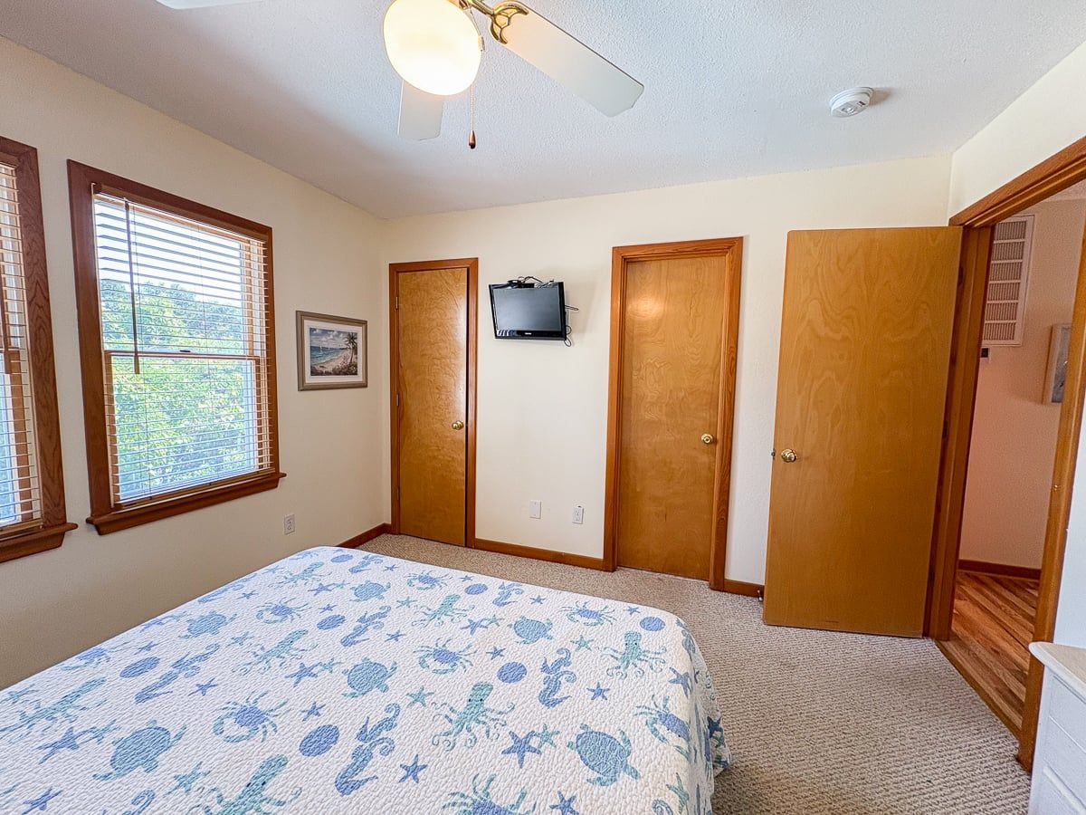 A bedroom with a bed, a ceiling fan, a TV, and a door.