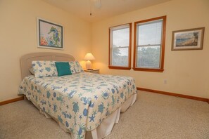 A bedroom with a bed, two windows, a nightstand, and a lamp.