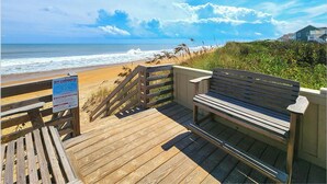 Una passerella di legno che conduce a una spiaggia, con una panchina e un cartello che avvisa sui pericolosi effetti delle correnti marine.