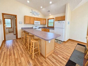 A kitchen with wooden cabinets, a central island with stools, a microwave, and a refrigerator.