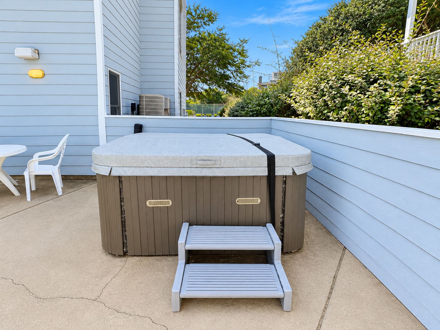 A hot tub with a step, two white plastic chairs, and a concrete patio.